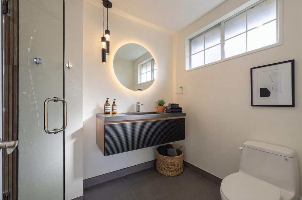 Bathroom with a floating dark vanity, round backlit mirror and a glass walk in shower